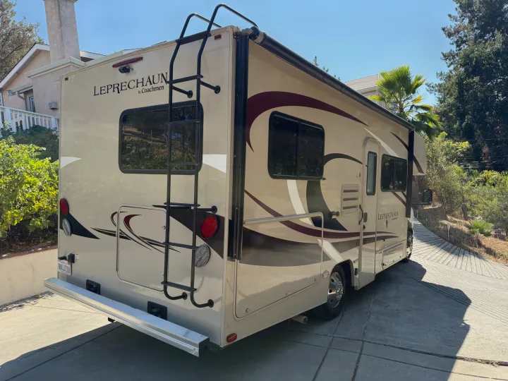 Beige and brown Class C LEPRECHAUN by Coachmen RV rental with a rear ladder and side awning, parked on a driveway.. Forest River Coachmen Leprechaun 2020