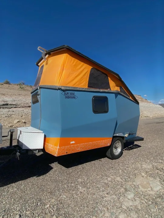 This unique blue & orange pop-top camper trailer, ideal for an RV rental, is parked in a rocky desert under a clear blue sky.. Cricket standard 2013