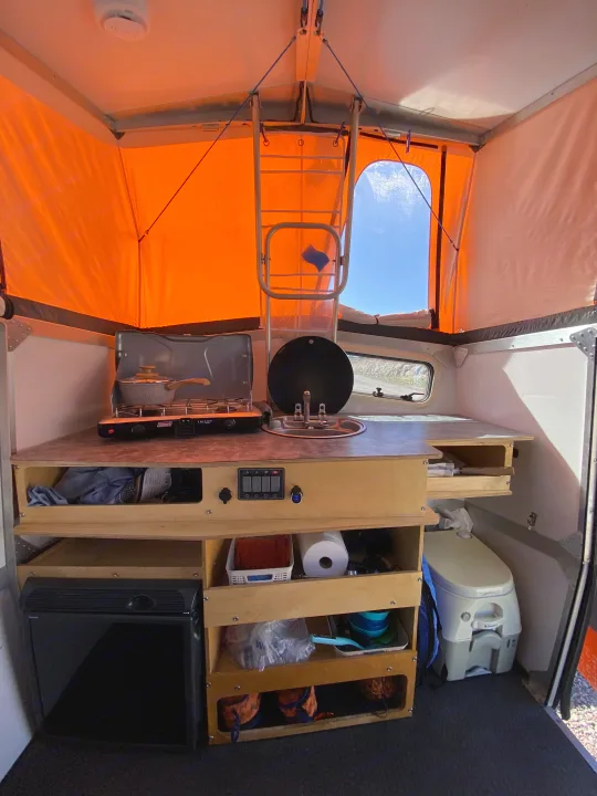 This RV rental camper interior features a compact kitchen (stove, sink), ample storage, a portable toilet, and a mini-fridge.. Cricket standard 2013