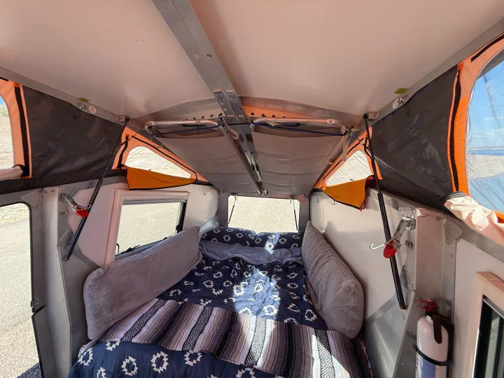 Inside an RV rental pop-up camper, showcasing a cozy bed with blankets, overhead storage, and a fire extinguisher.. Cricket standard 2013