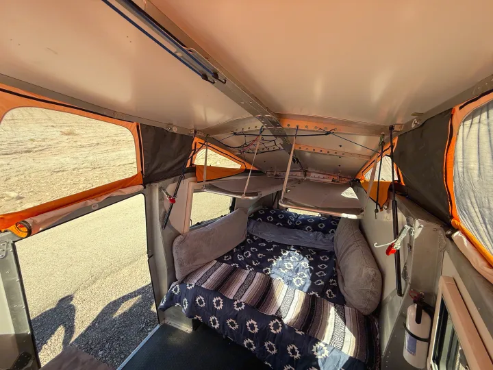 Cozy rv rental interior with a bed, two bunk beds, and windows showing outdoor landscape. A fire extinguisher is mounted inside.. Cricket standard 2013