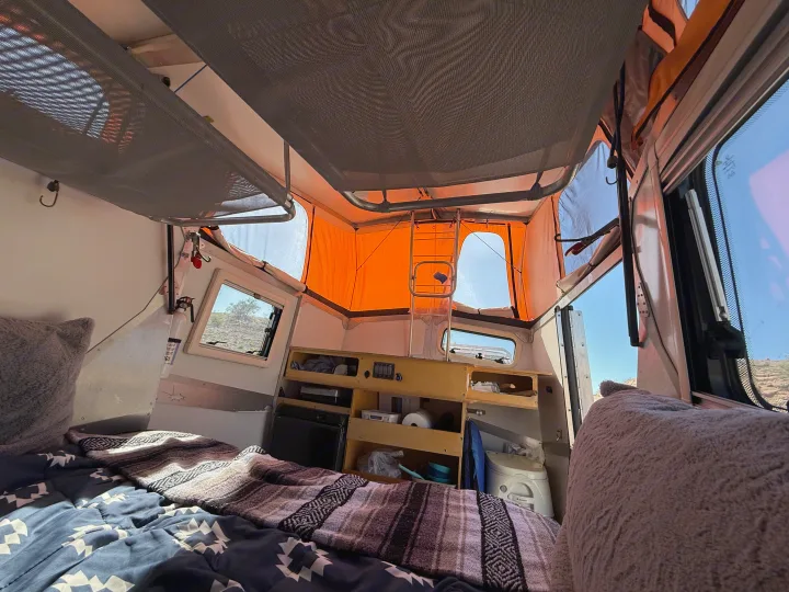 Cozy RV rental interior with bed, storage, and portable toilet. A pop-top roof opens to the sunny outdoors, ready for adventure!. Cricket standard 2013