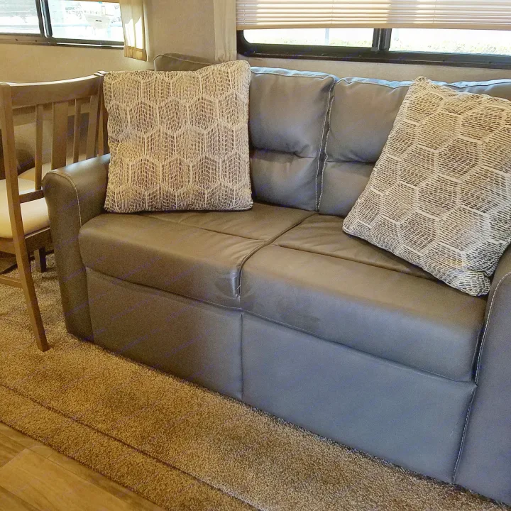 Enjoy this comfortable dark sofa with patterned pillows in an RV rental living space, showing carpet, wood floor, and windows.. Coachmen Catalina 2021