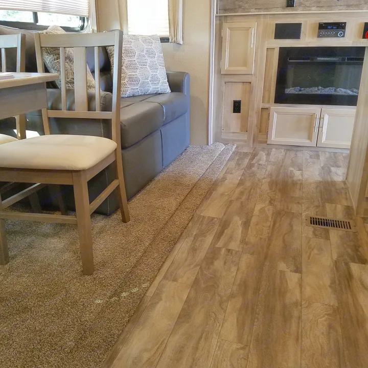 RV rental interior: dining area, sofa, entertainment center with electric fireplace, and carpet to wood-look floor.. Coachmen Catalina 2021