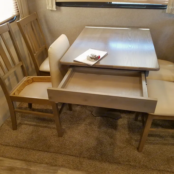 RV rental dining area with wooden table, open drawer, chairs (one missing cushion), and bench. Notepad and tape measure on table.. Coachmen Catalina 2021