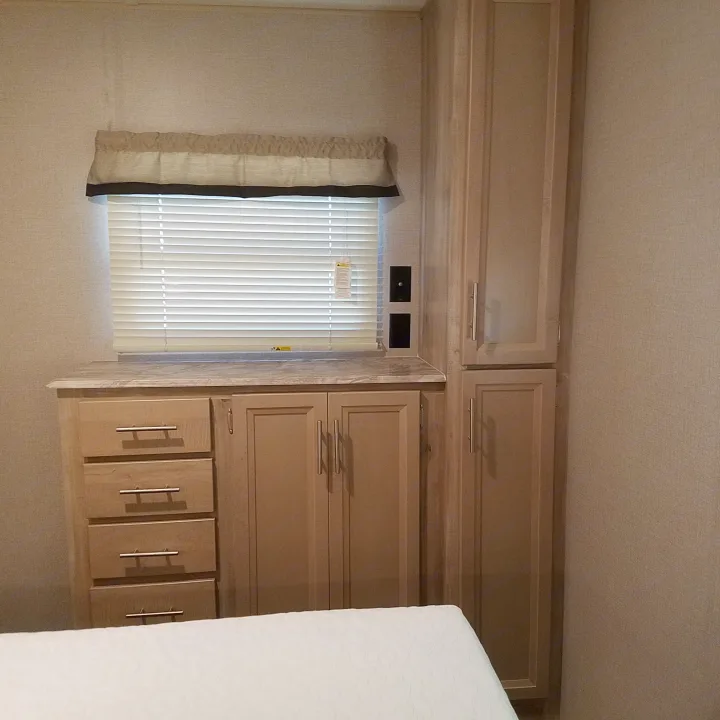 Compact RV rental bedroom with a window, under-window dresser/cabinets, and tall wardrobe storage.. Coachmen Catalina 2021