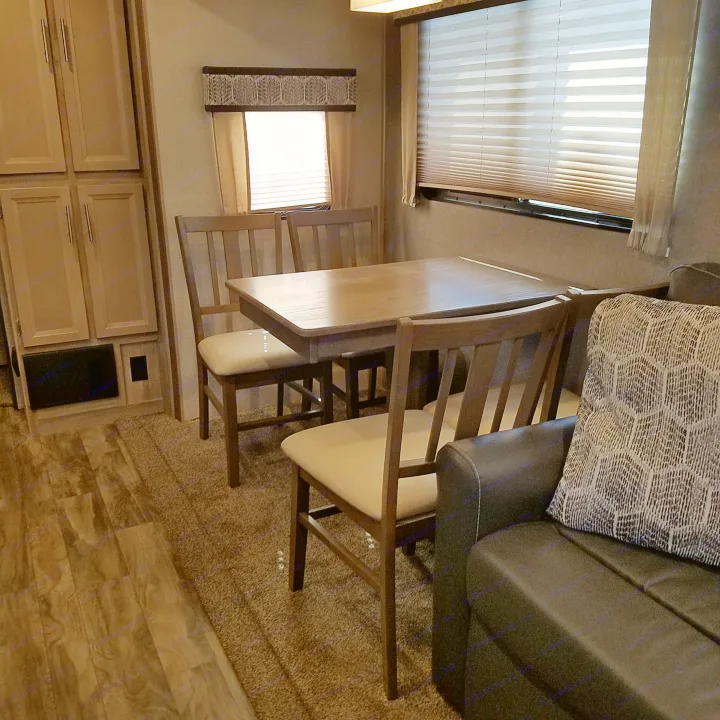 RV rental interior: dining area with wooden table, four chairs, light wood cabinets, windows, and a sofa.. Coachmen Catalina 2021