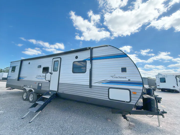 Modern Coachmen Catalina travel trailer, ideal for an RV rental adventure, parked on a gravel lot under a blue sky.. Coachmen Catalina 2021