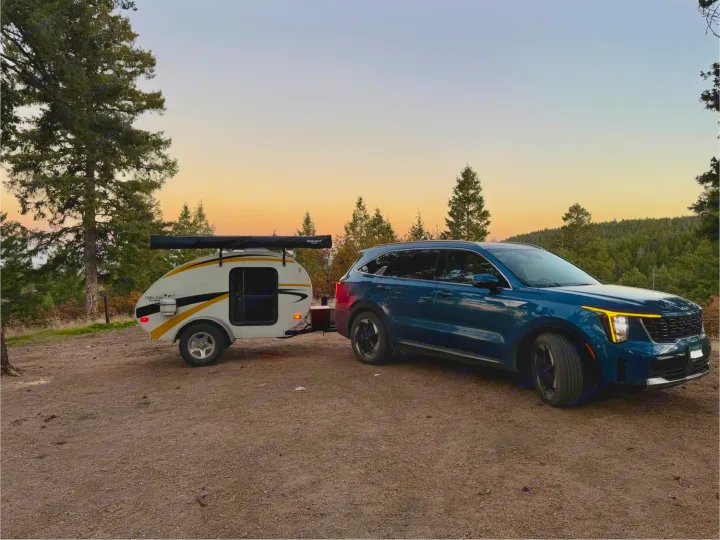 Serene dusk scene: Blue SUV towing a 'Little Guy' teardrop RV rental, ready for a forest camping getaway.. Lil’ Guy RET 2006