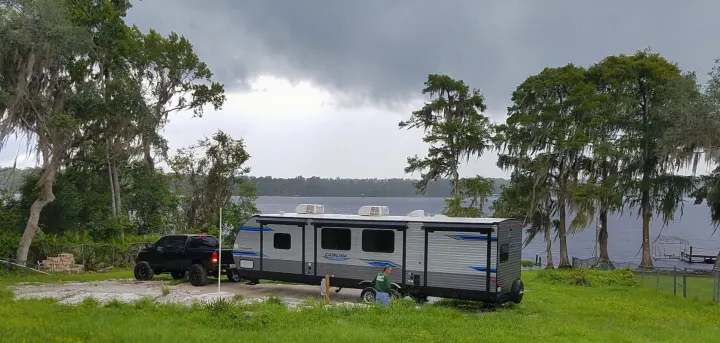 Scenic RV rental parked lakeside with a truck. Cloudy day, trees with Spanish moss, great for nature lovers.. Coachmen Catalina 2021