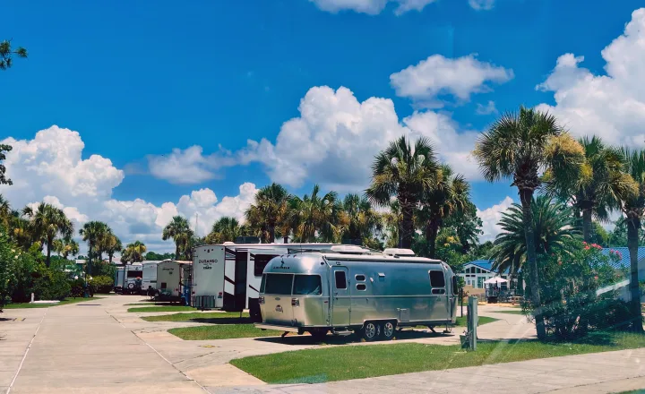 A bright day at an RV park, with an Airstream and other travel trailers parked among palm trees. Consider an RV rental!. Airstream Flying Cloud 2017