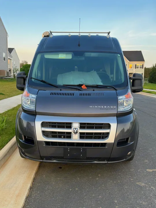Front view of a dark grey Winnebago Touring Coach RV rental, featuring a Dodge Ram logo, roof racks, and sunshade.. Winnebago Travato 2016