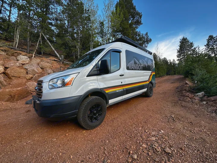 Adventure awaits with this RV rental! A white VANDOIT camper van on a rocky dirt road in a forest, ready for exploration.. Ford Transit 2018