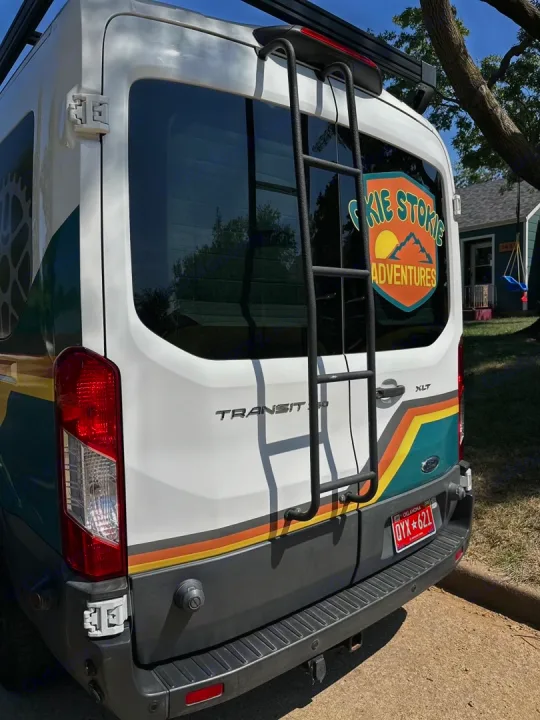 Rear view of an RV rental van, showcasing its ladder, "Sokie Stokie Adventures" logo, and colorful retro stripes.. Ford Transit 2018