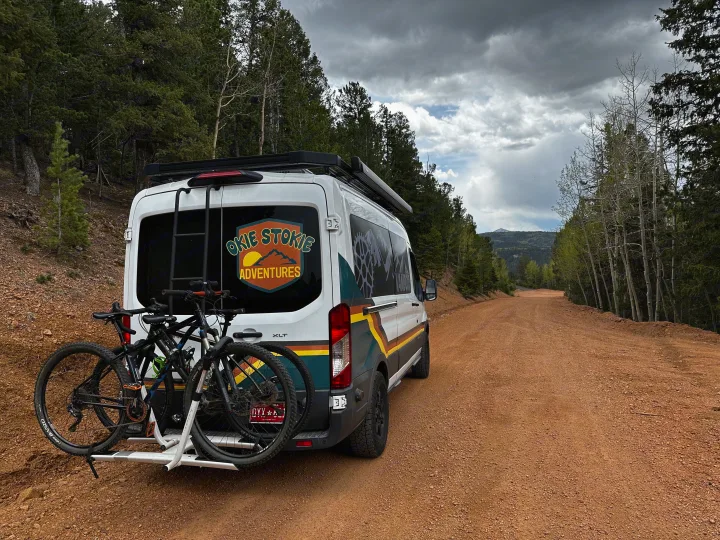 "Okie Stokie Adventures" RV rental van with mountain bikes parked on a gravel forest road.. Ford Transit 2018