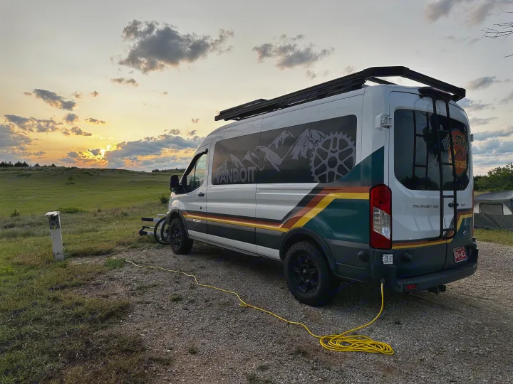 This "VANDOIT" rv rental camper van is parked at a scenic campsite during sunset, hooked up and ready for adventure.. Ford Transit 2018