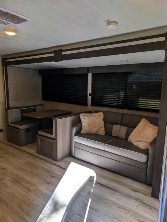 Modern RV rental interior featuring a cozy dinette, sofa, and light wood floors. Perfect for comfortable travel adventures.. Keystone RV Hideout 2025