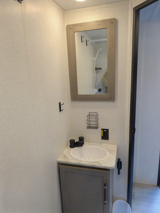 Compact RV rental bathroom with vanity, sink, mirror, wall hooks, storage, and a shower view.. Keystone RV Hideout 2025