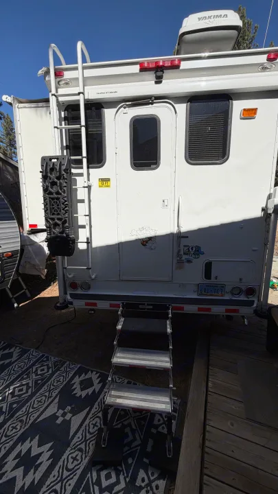 White rv rental camper's rear exterior shows a ladder, entry steps, a Yakima cargo box, and a Nevada license plate.. Ford F350 Diesel Double Cab 2017
