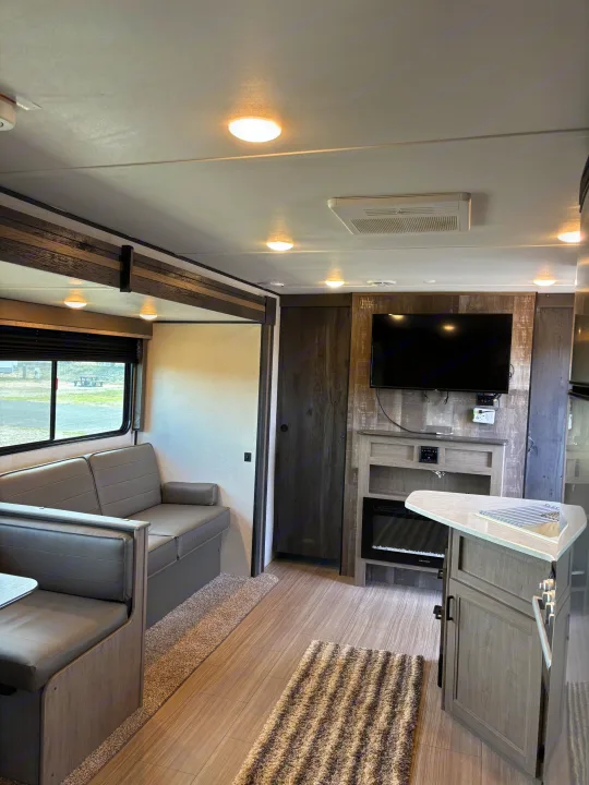 Cozy RV rental interior featuring a dinette, TV, fireplace, and kitchen area with modern finishes.. Keystone RV Hideout 2021