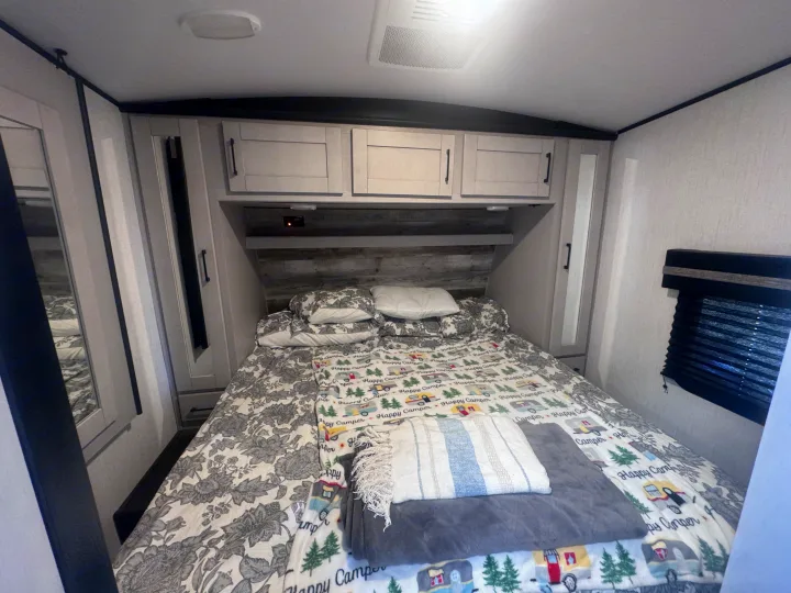 Cozy RV rental bedroom with a comfy bed, overhead cabinets, and window blinds. Perfect for camping trips!. Heartland Torque 2022