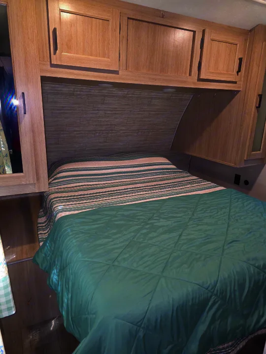 Cozy RV rental bedroom with a bed featuring green and striped bedding, light wood cabinets, and a modern plank-style headboard.. Coachmen Catalina Legacy 2024