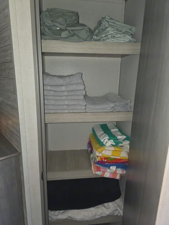 Organized RV rental closet with green sheets, stacked white towels, colorful beach towels, and a black cushion on the bottom.. Coachmen Catalina Legacy 2024