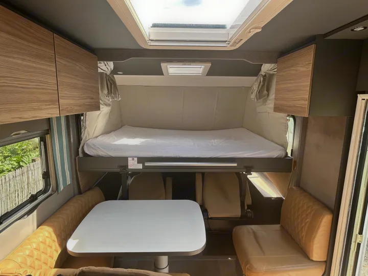 This RV rental interior features a clever drop-down bed over a dining area, with a large skylight above.. GlamperRV DBM Automatic 2025