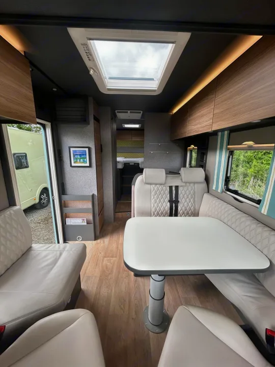 Explore this modern RV rental interior featuring a bright skylight, comfortable dining area with light seating, and wooden accents.. GlamperRV DBM Automatic 2025