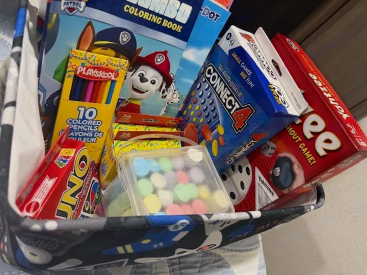RV rental activities: Kids' basket with Paw Patrol coloring, pencils, UNO, Connect 4, Yahtzee, & candies for travel fun.. Grand Design Transcend 2025
