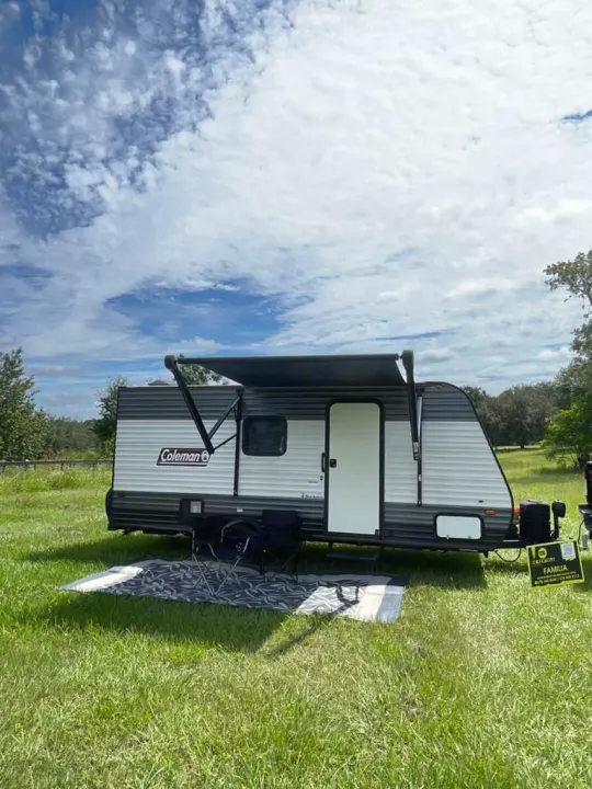 Coleman RV rental parked in a grassy field with an extended awning and chairs, ready for outdoor adventures.. LANTERN 17B 2021