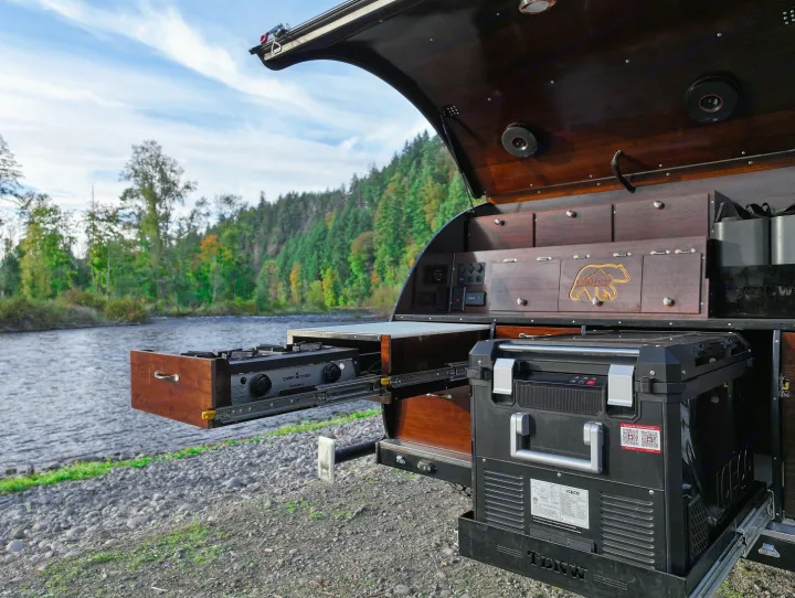 RV rental: A camper's open kitchen, featuring a pull-out stove and fridge, set against a beautiful river and forest backdrop.. Teardrops NW Ranger 2025