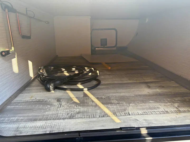 RV rental's spacious storage bay with a coiled power cord, crank handle, and durable wood-look flooring.. Heartland RVs North Trail 2021