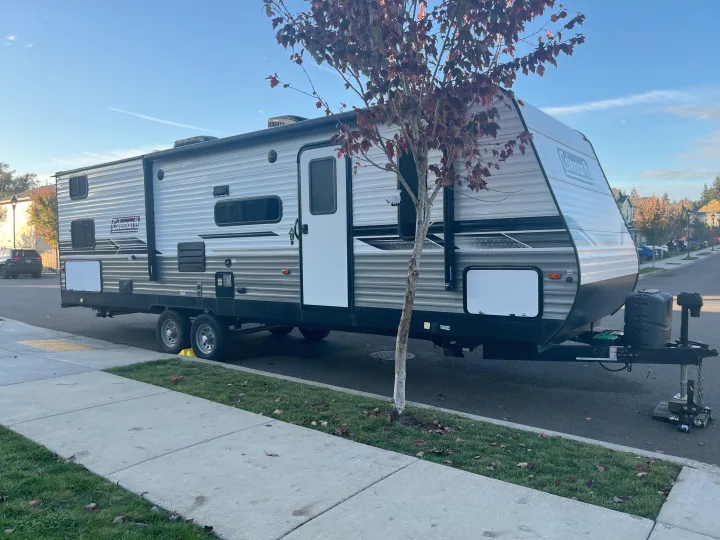 A grey and black Coleman RV rental travel trailer is parked on a street, ready for camping trips and outdoor adventures.. Dutchmen Coleman Lantern 2022