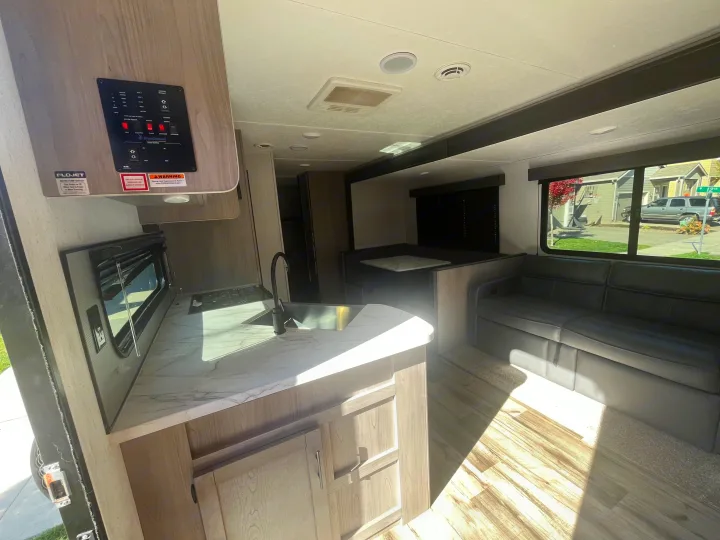 Inside an RV rental: a bright living space with a kitchen, dining booth, and sofa by the window, ready for adventure.. Dutchmen Coleman Lantern 2022