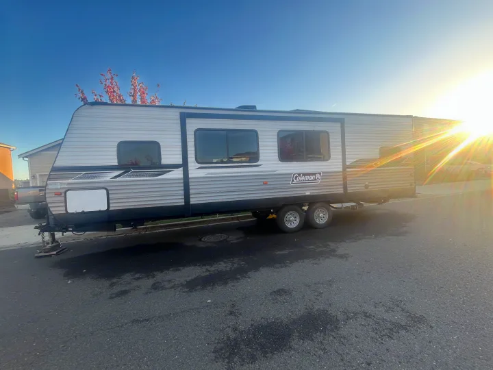 Modern grey Coleman travel trailer RV rental, parked on a street on a bright, sunny day.. Dutchmen Coleman Lantern 2022