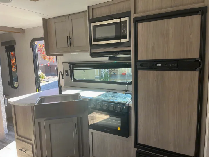 This RV rental kitchen features light wood cabinets, a farmhouse sink, microwave, oven, and fridge, perfect for your next adventure.. Dutchmen Coleman Lantern 2022