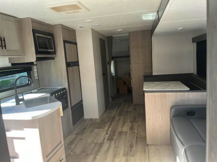 Modern rv rental interior with a full kitchen, dinette seating, and rear bunk bed area. Light wood and gray accents.. Dutchmen Coleman Lantern 2022