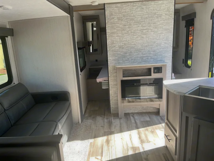 Spacious RV rental interior featuring a living area with a dark sofa, a fireplace, a kitchen counter with a sink, and a bedroom entrance.. Dutchmen Coleman Lantern 2022