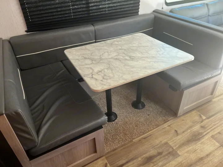 This modern RV rental dinette features U-shaped grey seating, a marbled table, a carpeted area, and a wood-look floor.. Dutchmen Coleman Lantern 2022