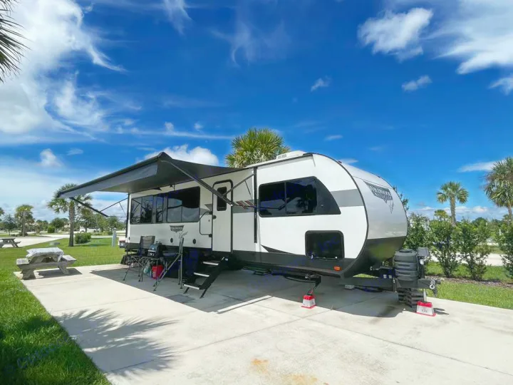 Sunny day at the campground with a spacious RV rental, complete with awning and outdoor seating.. wildwood 28 view 2025