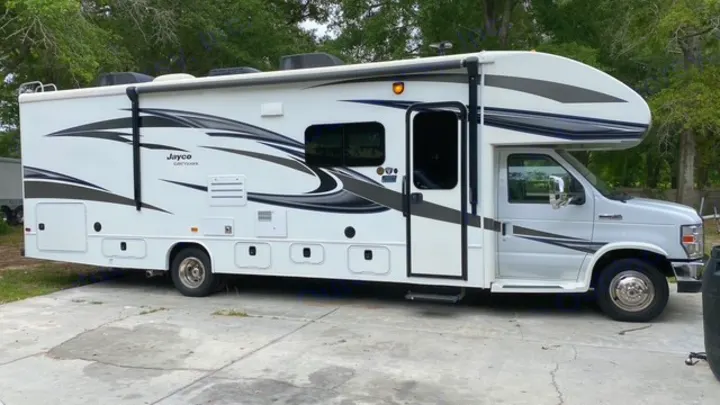 A white Jayco Greyhawk RV, featuring stylish gray and black graphics, is parked on concrete, ready for your next rv rental trip.. Jayco Greyhawk 2019