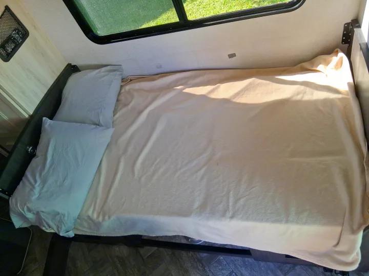 Inside an **rv rental**: Compact bedroom with a bed, light bedding, and window showing greenery.. Forest River SLE 2021
