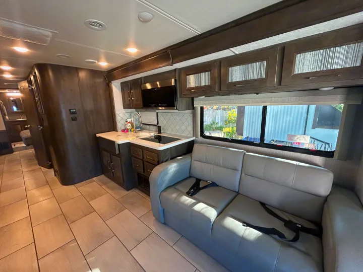 Modern RV rental interior with a gray sofa, compact kitchen, wood-look cabinets, and sleek tile flooring.. Forest River Coachmen Sportscoach RD 2021