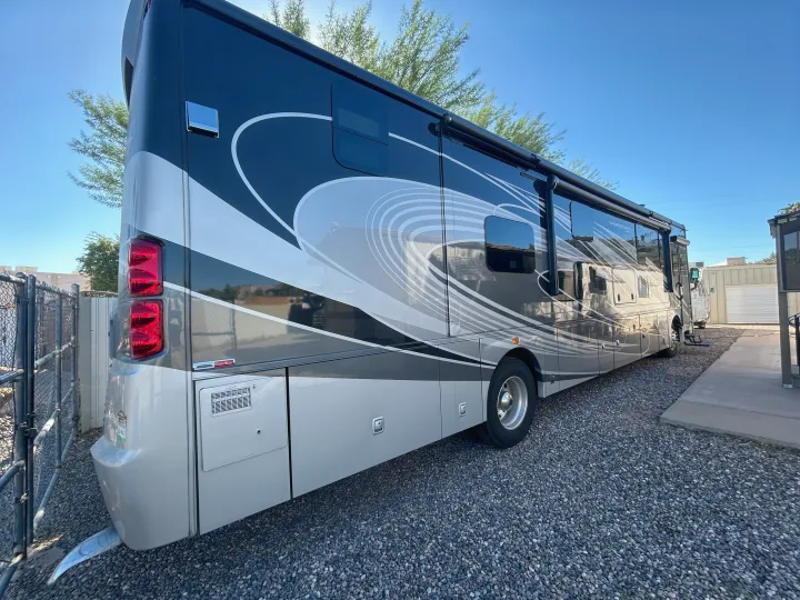 A luxurious black & silver rv rental, showcasing its rear and side with stylish swirl graphics, is parked on a gravel lot.. Forest River Coachmen Sportscoach RD 2021