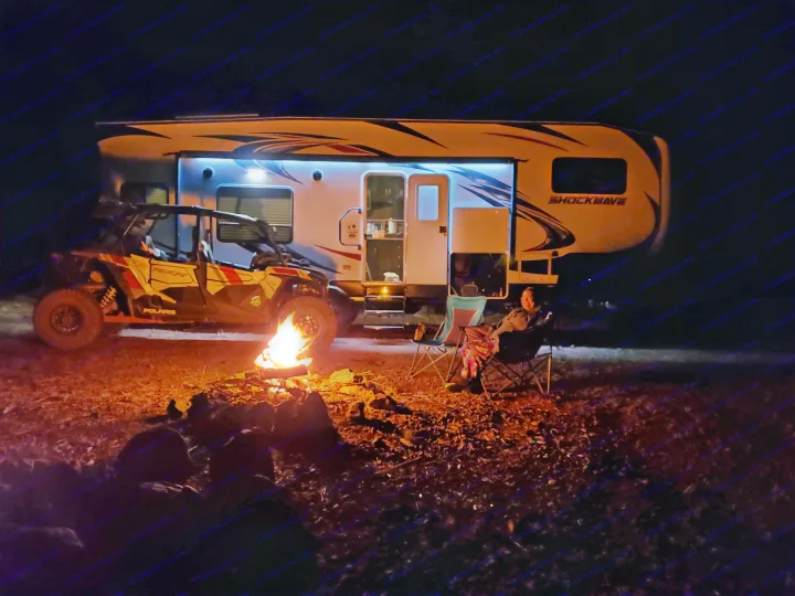 Night camping: RV rental, Polaris UTV, and a cozy campfire. A person enjoys the outdoor evening by their RV.. Forest River Shockwave 2018