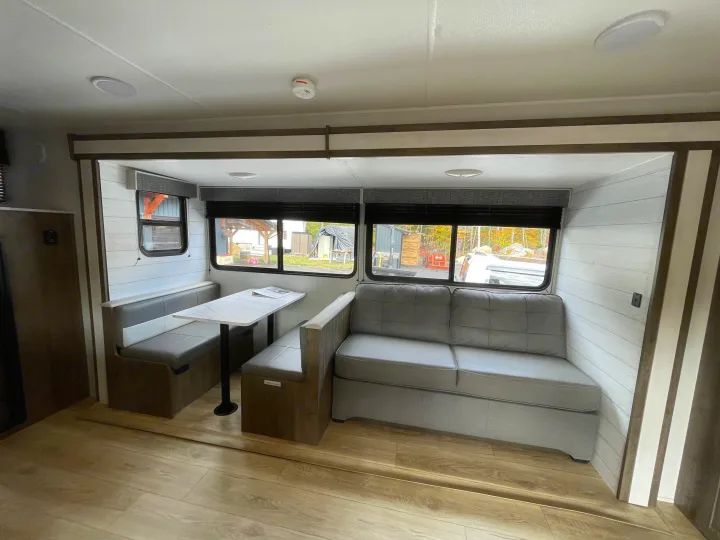 Cozy RV rental interior with a grey dinette and sofa, light wood floor, and shiplap walls, offering a comfortable living space.. Heartland Pioneer 2024