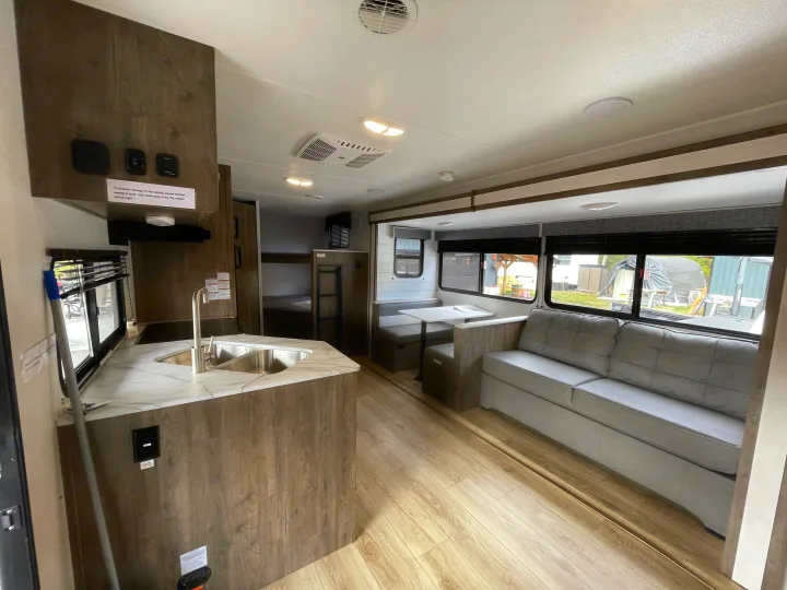 Bright RV rental interior: kitchen with sink, dining booth, sofa, and bunk beds visible in the rear.. Heartland Pioneer 2024