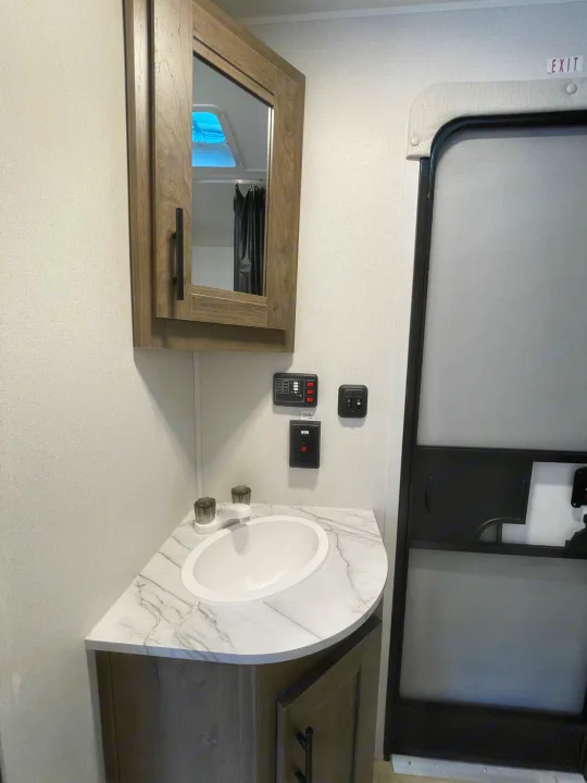 Compact rv rental bathroom featuring a sink, mirrored medicine cabinet, control panel, and the exit door.. Heartland Pioneer 2024