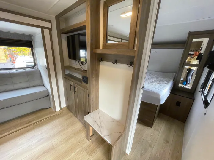 Modern rv rental interior: bright space with gray sofa, TV, cabinets, coat hooks, and comfortable bed beyond.. Heartland Pioneer 2024